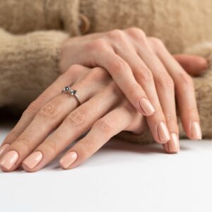 Graceful thin fingers of a girl with a trendy pastel nude manicure and a fluffy soft sweater and a cute silver ring bow